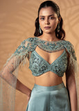 Woman wearing a teal embroidered blouse with sheer sleeves against a beige background
