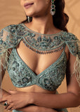 Woman wearing a intricately designed green blouse with embroidery and embellishments.
